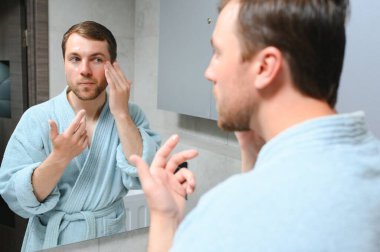 Yakışıklı genç adam banyoda yüzüne krem sürüyor..