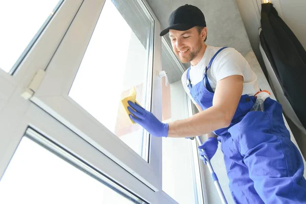 Male professional cleaning service worker in overalls cleans the windows