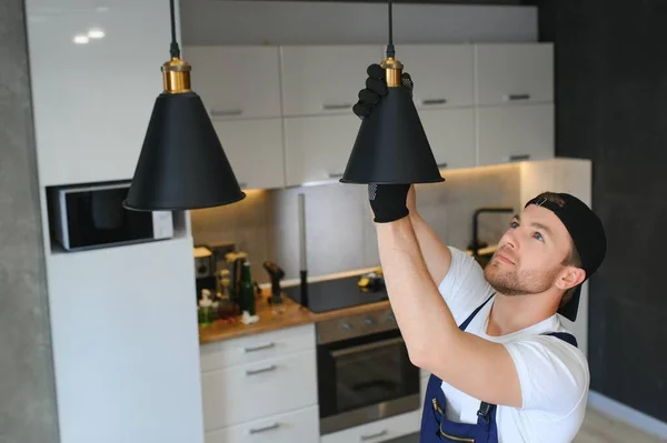 A male electrician changes the light bulbs in the ceiling light. men\'s household duties. care of electrical appliances at home.