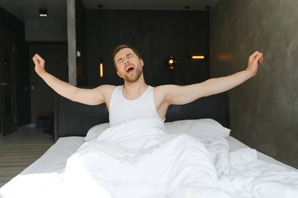 stock image Young man sleeping waking up and stretching in his bed.