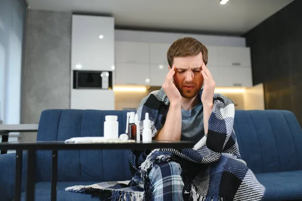 Man wrapped in plaid on the sofa feeling sick illness at home.