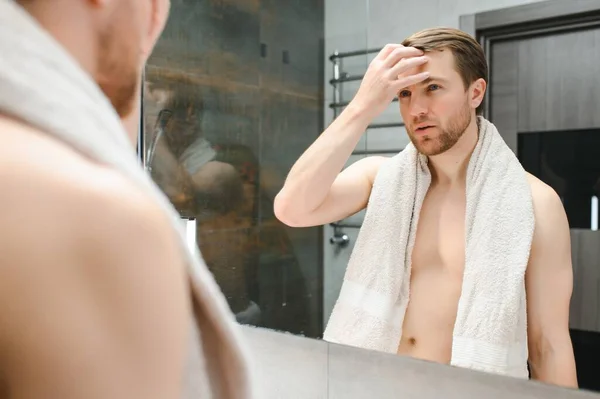 Young man looking in mirror after shaving at home.