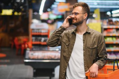 Süpermarkette alışveriş yapan yakışıklı adam, gülümseyen, telefon kullanan.