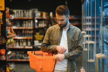 Yakışıklı genç adam süpermarkette yemek seçiyor.