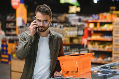 Süpermarkette alışveriş yapan yakışıklı adam, gülümseyen, telefon kullanan.