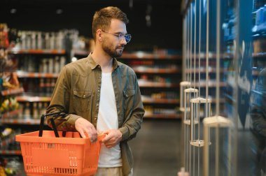 Yakışıklı adam bakkal gıda ürünleri Başlangıç rafı seçme süpermarkette alışveriş gülümseyen portresi.