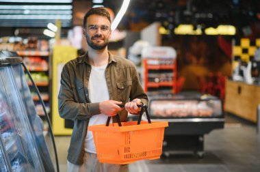 Yakışıklı genç adam süpermarkette yemek seçiyor.