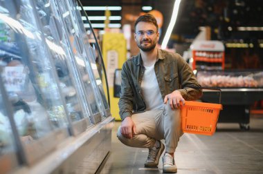 Yakışıklı adam bakkal gıda ürünleri Başlangıç rafı seçme süpermarkette alışveriş gülümseyen portresi.