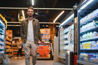 Genç adam süpermarketten alışveriş yapıyor. Arka plandaki diğer müşteriler. Tüketim kavramı