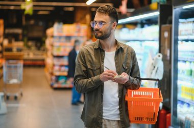 Yakışıklı genç adam süpermarkette yemek seçiyor.