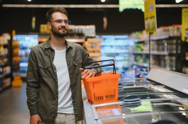 Yakışıklı genç adam süpermarkette yemek seçiyor.