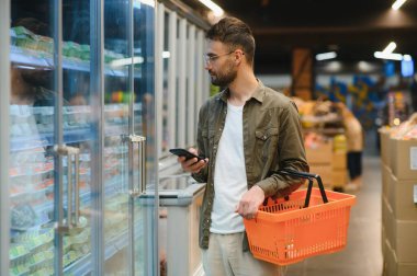 Süpermarkette alışveriş yapan yakışıklı adam, gülümseyen, telefon kullanan.