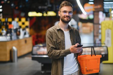 Yakışıklı adam, modern süpermarketten ya da marketten sağlıklı yiyecek ve içecek alıyor. Yaşam tarzı ve tüketim konsepti.