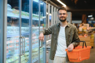 Yakışıklı genç adam süpermarkette yemek seçiyor.
