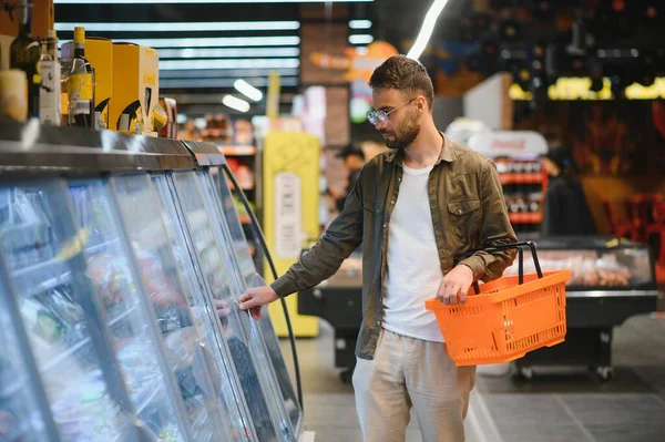 Handsome man buying some healthy food and drink in modern supermarket or grocery store. Lifestyle and consumerism concept.