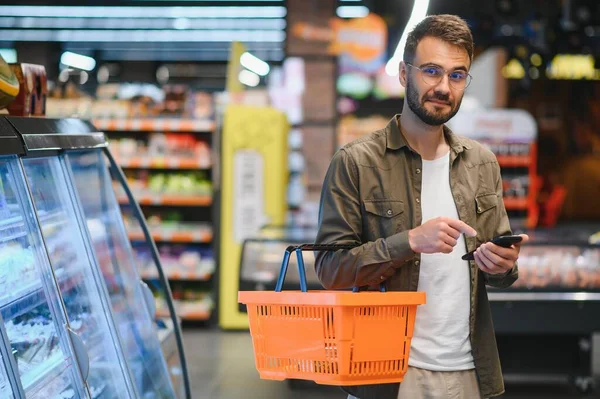 Süpermarkette alışveriş yapan yakışıklı adam, gülümseyen, telefon kullanan.