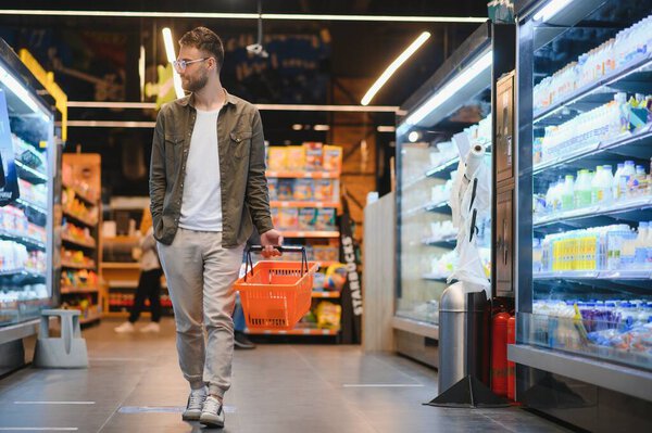 Portrait of smiling handsome man grocery shopping in supermarket, choosing food products from shelf.