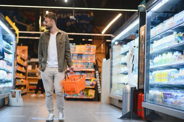 Young man buying groceries at the supermarket. Other customers in background. Consumerism concept