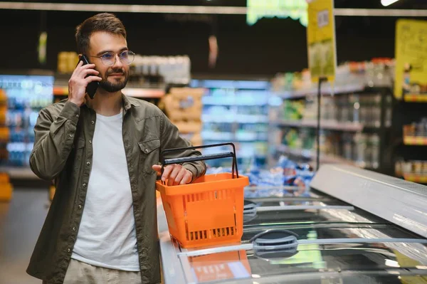 Happy man buying healthy food and drink in a modern supermarket and talking on phone