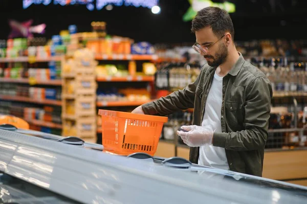 Young man buying groceries at the supermarket. Other customers in background. Consumerism concept