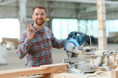 Elektrikli testere ile ahşap kesme masası. Marangozluk fabrikasında ahşap tahta kesen üniformalı profesyonel bir marangoz. Testere makinesi.