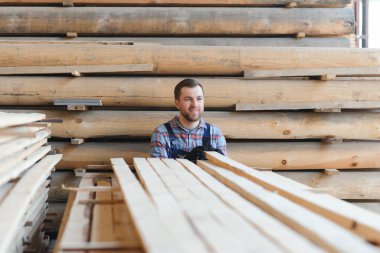 İnşaatçının elinde tahta kalaslar var. Konsept - kereste satışı. İnşaatçı ahşap tahtaları düşünüyor. Tahta işleme işi. Tahta kereste yığını.