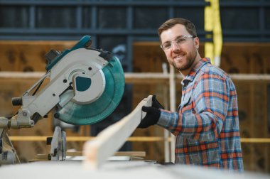 Ahşap bıçkıhanede elektrikli testere ile tahta kesme konusunda usta bir dolap ustası. Profesyonel dolap yapımcısı kereste fabrikasında testere kullanıyor. Ahşap mobilya üretimi