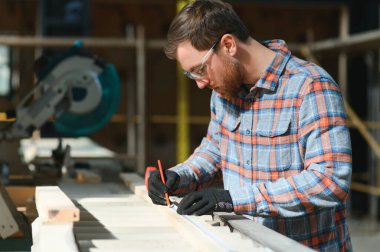 Profesyonel marangoz kereste fabrikasında tahta kesmek için testere makinesi kullanıyor. Marangozluk atölyesinde elektrikli testere ile çalışan yetenekli bir dolap yapımcısı. Erkek katılımcı, ahşap üretim tezgahı