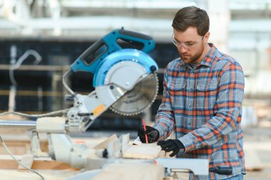 Elektrikli testere ile ahşap kesme masası. Marangozluk fabrikasında ahşap tahta kesen üniformalı profesyonel bir marangoz. Testere makinesi.