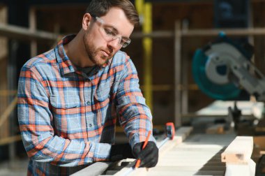 Elektrikli testere ile ahşap kesme masası. Marangozluk fabrikasında ahşap tahta kesen üniformalı profesyonel bir marangoz. Testere makinesi.