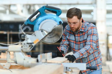 Profesyonel marangoz kereste fabrikasında tahta kesmek için testere makinesi kullanıyor. Marangozluk atölyesinde elektrikli testere ile çalışan yetenekli bir dolap yapımcısı. Erkek katılımcı, ahşap üretim tezgahı