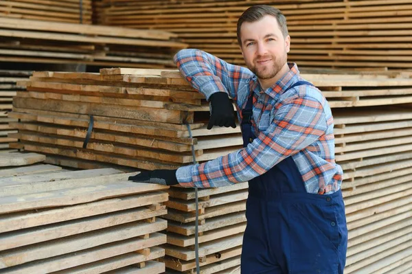 Industrial warehouse of a sawmill, an employee puts his hands on the finished products at the sawmill in the open air