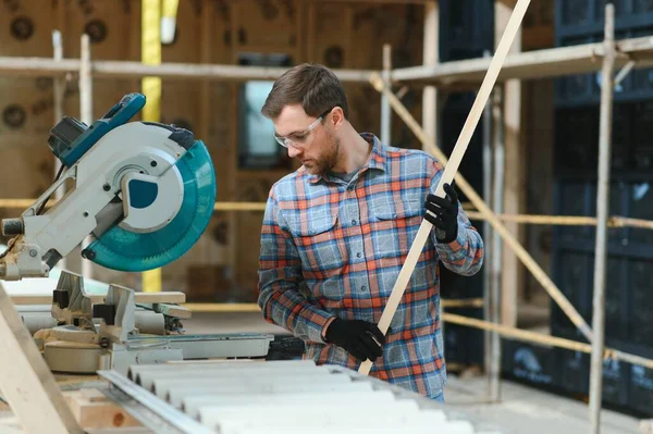 Profesyonel marangoz kereste fabrikasında tahta kesmek için testere makinesi kullanıyor. Marangozluk atölyesinde elektrikli testere ile çalışan yetenekli bir dolap yapımcısı. Erkek katılımcı, ahşap üretim tezgahı