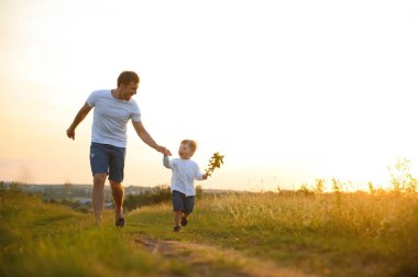 Babalar günü. Oynama ve doğa üzerinde günbatımında gülerek mutlu aile baba ve yürümeye başlayan çocuk evlat.