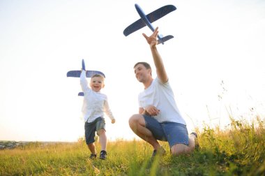 Şirin küçük çocuk ve yakışıklı genç babası parkta oyuncak bir uçakla oynarken gülümsüyorlar.