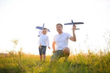 Şirin küçük çocuk ve yakışıklı genç babası parkta oyuncak bir uçakla oynarken gülümsüyorlar.