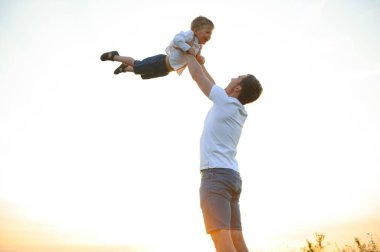 Babalar günü. Oynama ve doğa üzerinde günbatımında gülerek mutlu aile baba ve yürümeye başlayan çocuk evlat.