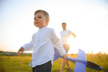Baba ve oğlu gün batımında doğada. Bir baba oğluyla gün batımında oyuncak uçaklarla oynar. Babalar Günü.