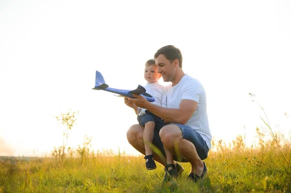 stock image Cute little boy and his handsome young dad are smiling while playing with a toy airplane in the park