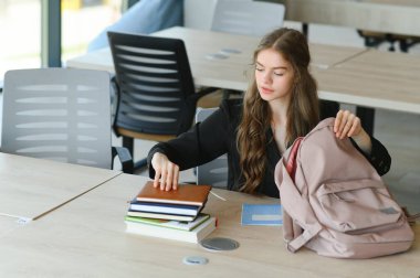 15 yaşında tatlı bir liseli kız elinde defterler, kitaplar ve derslerle okul masasında oturuyor..