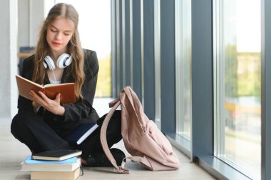 Kız gülümsüyor. Pencere ve okuma kitabı yakın otururken gülümseyen güzel liseli.