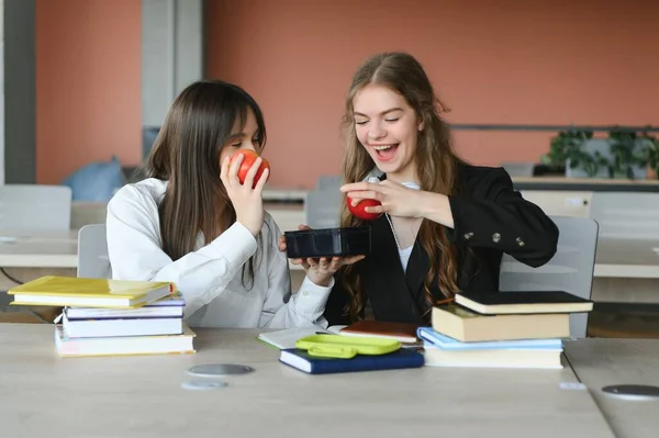 Ένα Χαριτωμένο Κορίτσι Χαμογελά Στην Συμμαθήτριά Της Ενώ Τρώει Μεσημεριανό — Φωτογραφία Αρχείου