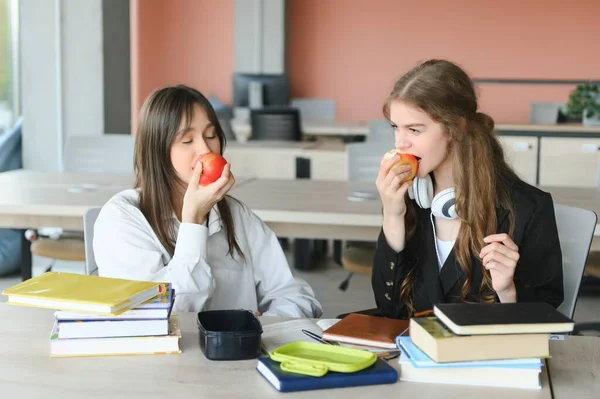 Ένα Χαριτωμένο Κορίτσι Χαμογελά Στην Συμμαθήτριά Της Ενώ Τρώει Μεσημεριανό — Φωτογραφία Αρχείου