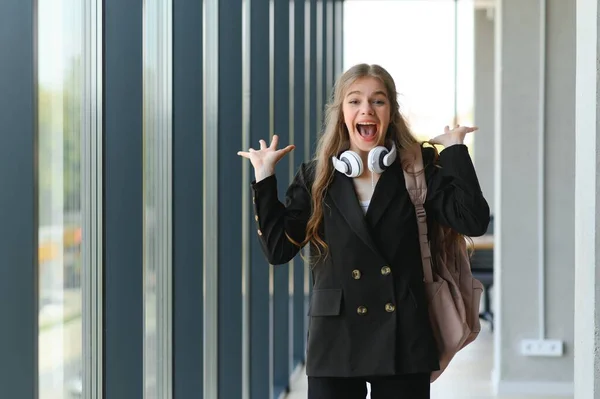 Emotional student girl within walls of institute celebrating successful exam pass, high school or college admission, european employee raised hands feels happy by salary growth, got promoted concept.