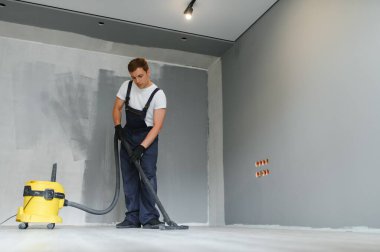 Elektrikli süpürge kullanan bir işçi inşaat kalıntılarını temizler. Bir işçi endüstriyel tesisleri temizliyor. çokgenler kullanılarak onarıldıktan sonra daire.
