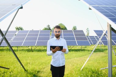 Fotovoltaik panellerin arka planında tableti olan erkek işçi güneş enerjisi santrali