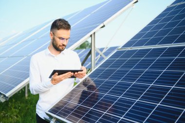 The portrait of a young engineer checks with tablet operation with sun, cleanliness on field of photovoltaic solar panels. Concept: renewable energy, technology, electricity, service, green power