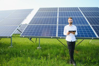 Fotovoltaik panellerin arka planında tableti olan erkek işçi güneş enerjisi santrali