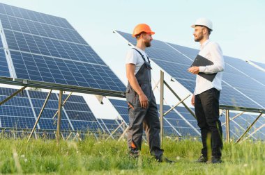 Güneş çiftliği (güneş paneli), iki mühendis ile birlikte sistemin işleyişini kontrol etmek için yürür, dünyanın enerjisini korumak için alternatif enerji, temiz enerji üretimi için fotovoltaik modül fikri.