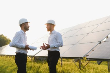 Güneş çiftliği (güneş paneli), iki mühendis ile birlikte sistemin işleyişini kontrol etmek için yürür, dünyanın enerjisini korumak için alternatif enerji, temiz enerji üretimi için fotovoltaik modül fikri.
